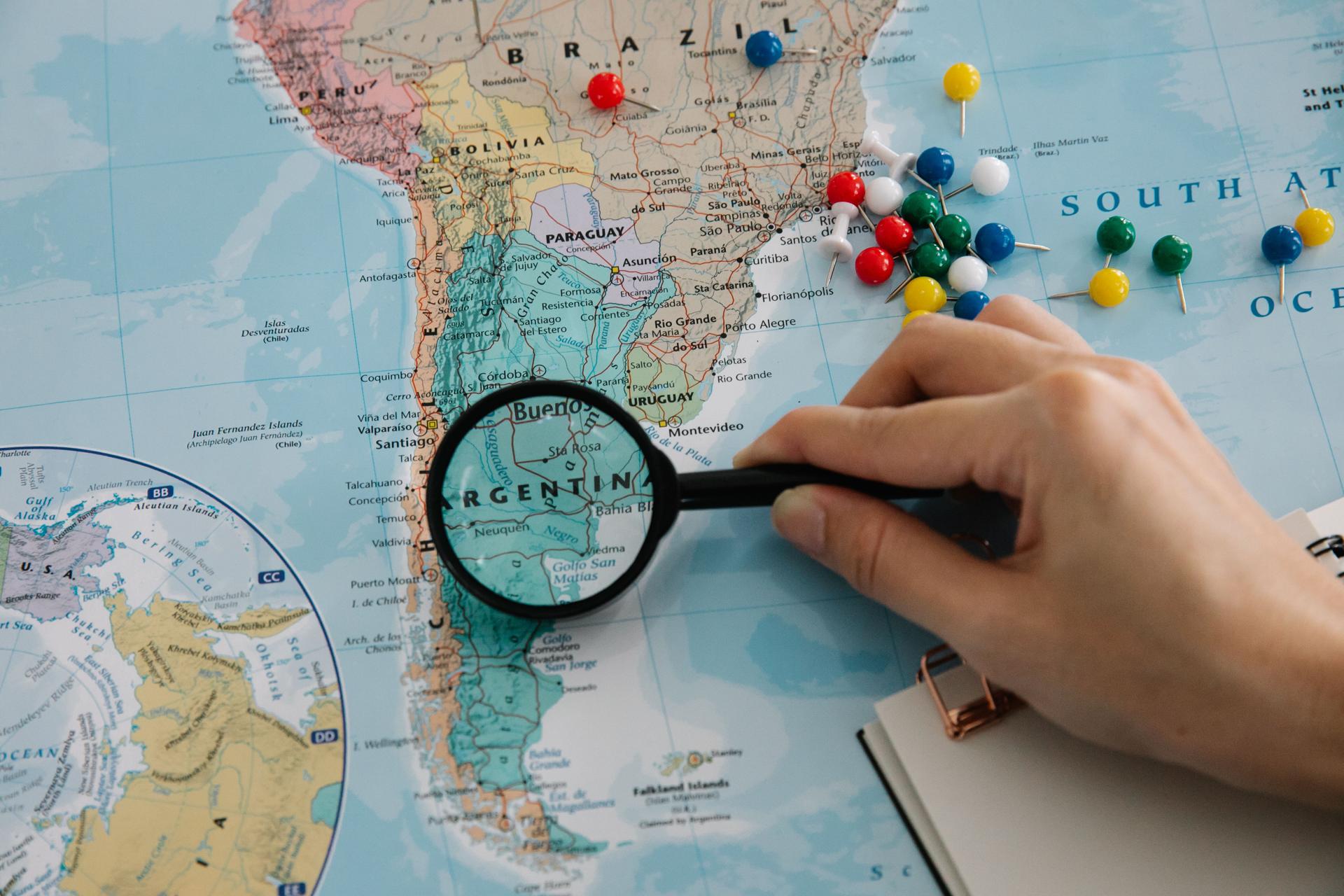 Hand with magnifying glass examining a map of South America for country-of-origin research